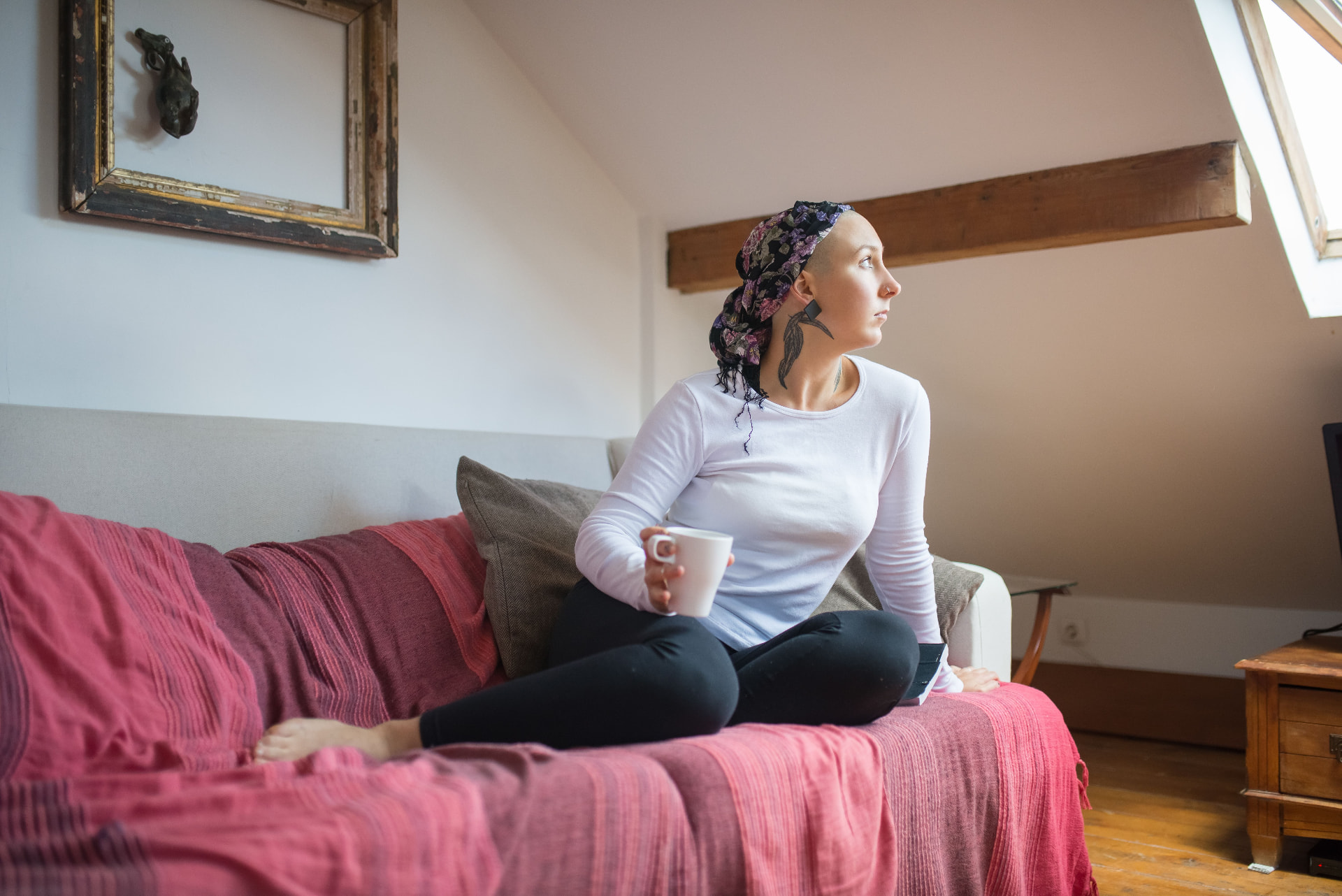A person recovering at home, sitting on a sofa with a warm drink in afternoon light